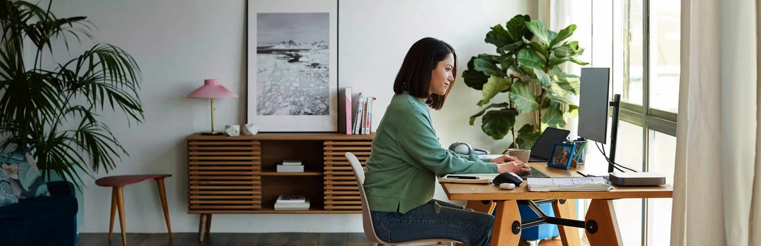 A woman sitting at her desk in front of a window, looking at her computer