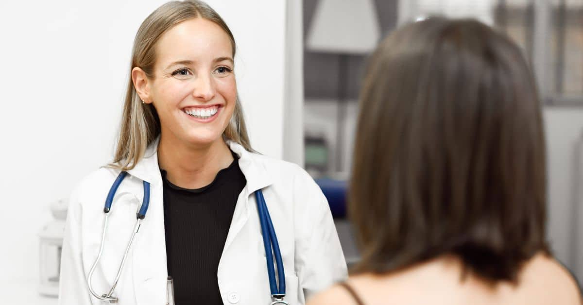 A doctor smiles at her patient in the foreground. Learn why DME compliance is key for healthcare professionals.